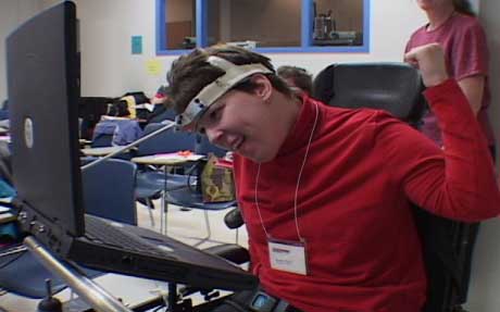 young woman in wheelchair using computer with headstick